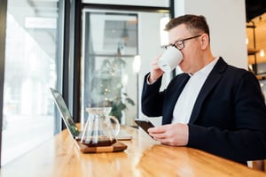 Man drinking a coffee and looking at his laptop on a desk. Photo by LinkedIn Sales Solutions on Unsplash.